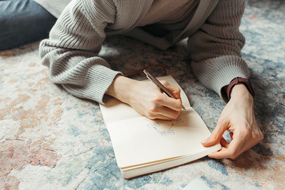 An adult writing a flowchart on a notebook while sitting on a colorful rug, fostering creativity and planning.