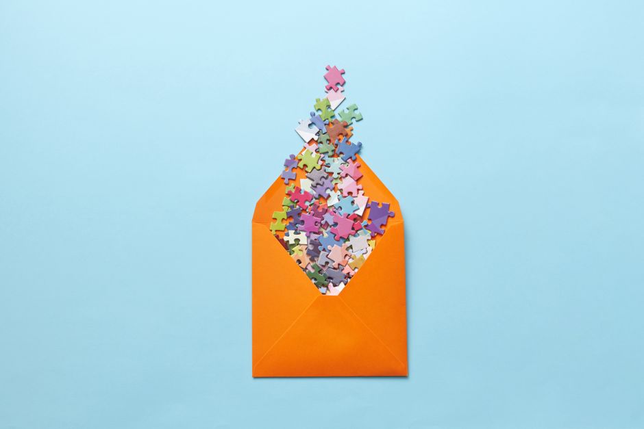 A vibrant collection of puzzle pieces spilling out of an orange envelope on a light blue background.